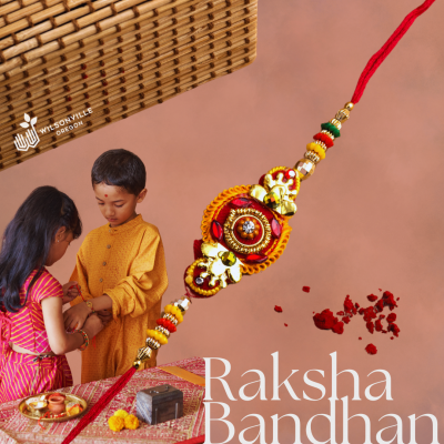 Image shows a sister tying a rakhi thread around her brothers wrist with text to the right of them that reads Raksha Bandhan