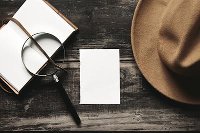 blank notebook with magnifying glass and fedora hat