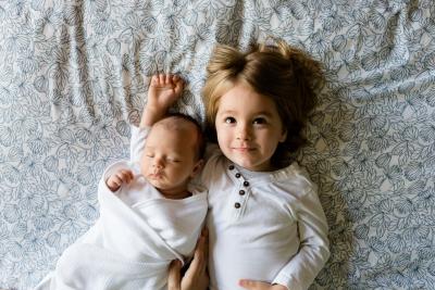 toddler and baby on bedsheet looking up at camera